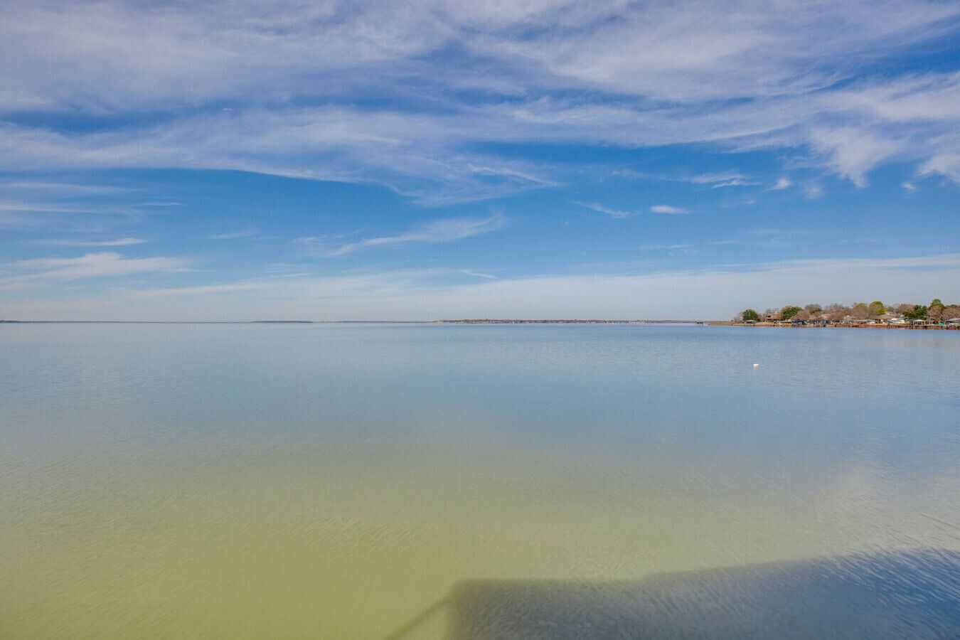A calm body of water with a clear sky and a distant shoreline with buildings.