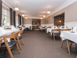 En restaurant med flere borde, stole og hængende pendellamper.