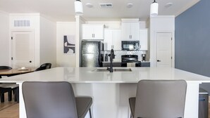 A modern kitchen with white cabinets, a stainless steel refrigerator, a microwave, and a large island with bar stools. - Landing Apartments - West Asheville (Asheville)