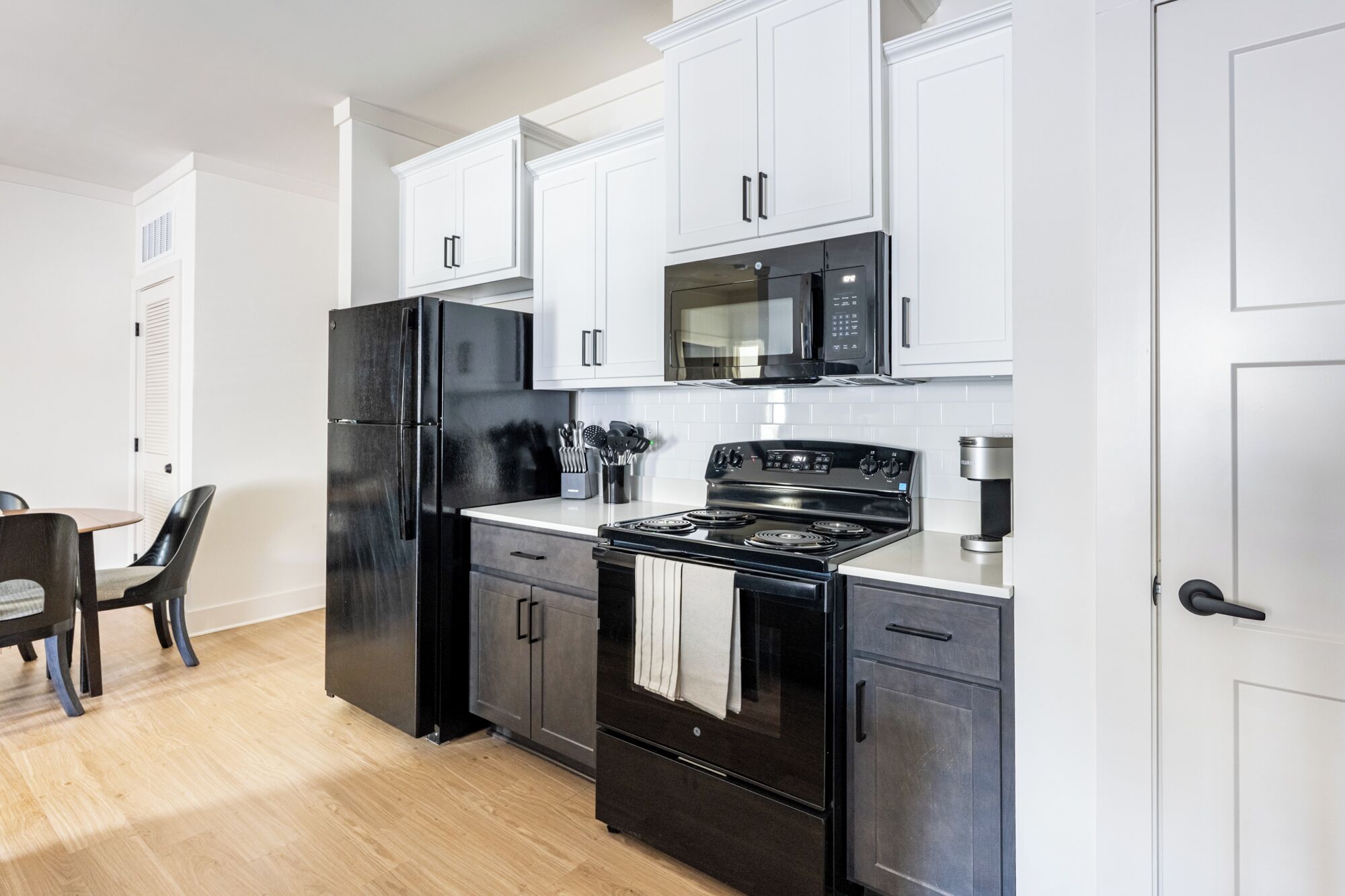 A modern kitchen with black appliances, white cabinets, and a wooden dining table.