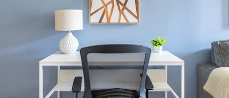 Ein modernes Zimmer mit Schreibtisch, Stuhl, Lampe, Pflanze und Wandbild.