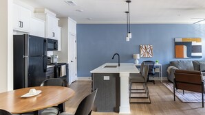 A modern kitchen with white cabinets, a black refrigerator, and a central island with a sink. - Landing Apartments - West Asheville (Asheville)