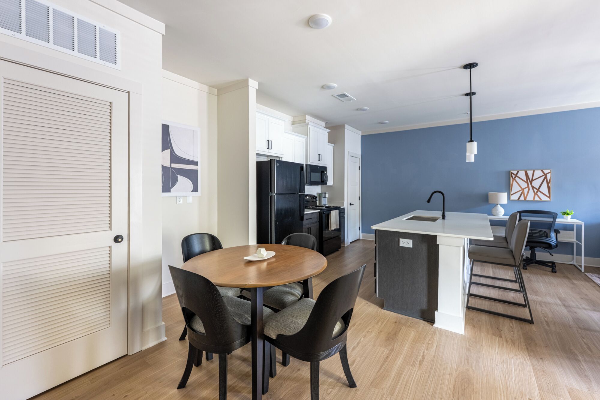 A modern kitchen with a central island, a dining area with a round table and chairs, and a blue accent wall.