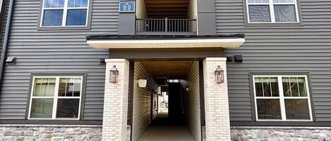 A multi-story building with a central entrance, a covered walkway, and a sign indicating a parking area.