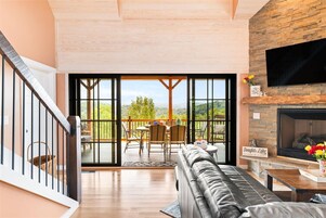 A spacious living area with a fireplace, a large TV mounted on the wall, and a balcony with a view of the outdoors.