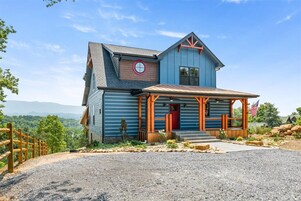 A two-story house with a blue exterior, a red door, and a porch with wooden railings.