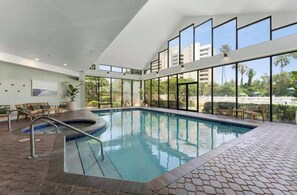 A modern indoor swimming pool with clear glass walls, a brick floor, and wooden lounge chairs. - New listing! 2/2 Apartment Close to Universal (Orlando)