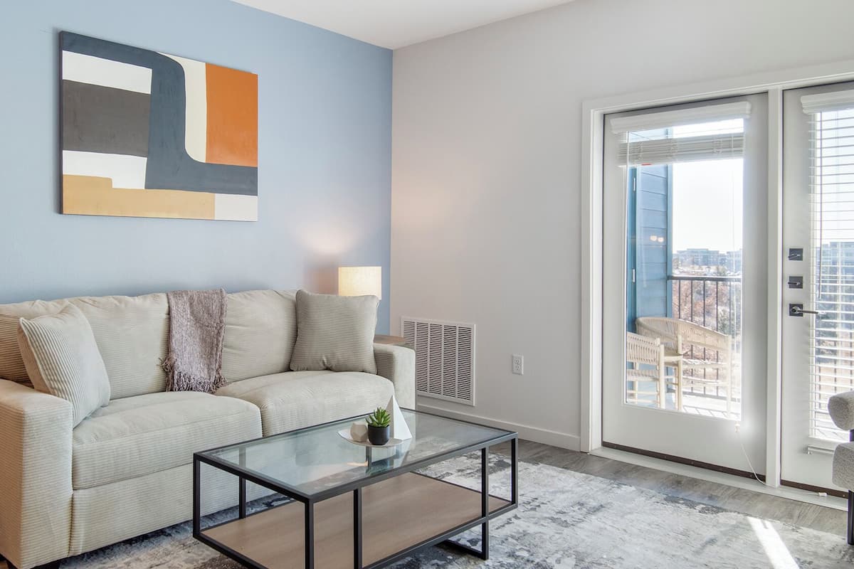 A living room with a sofa, a glass coffee table, and a city view through a sliding door.