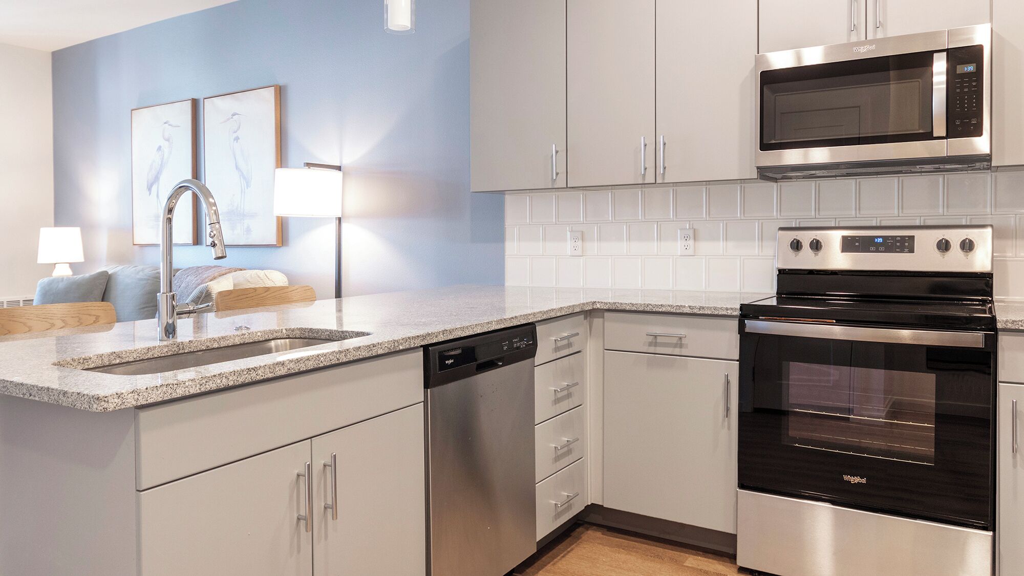 A modern kitchen with stainless steel appliances, white cabinetry, and a granite countertop.