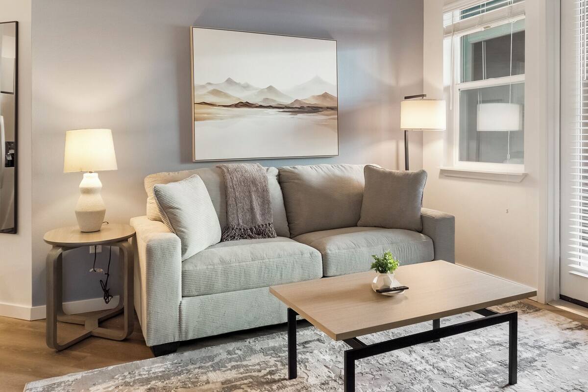 A modern living room with a sofa, a small table, a lamp, and a painting on the wall.