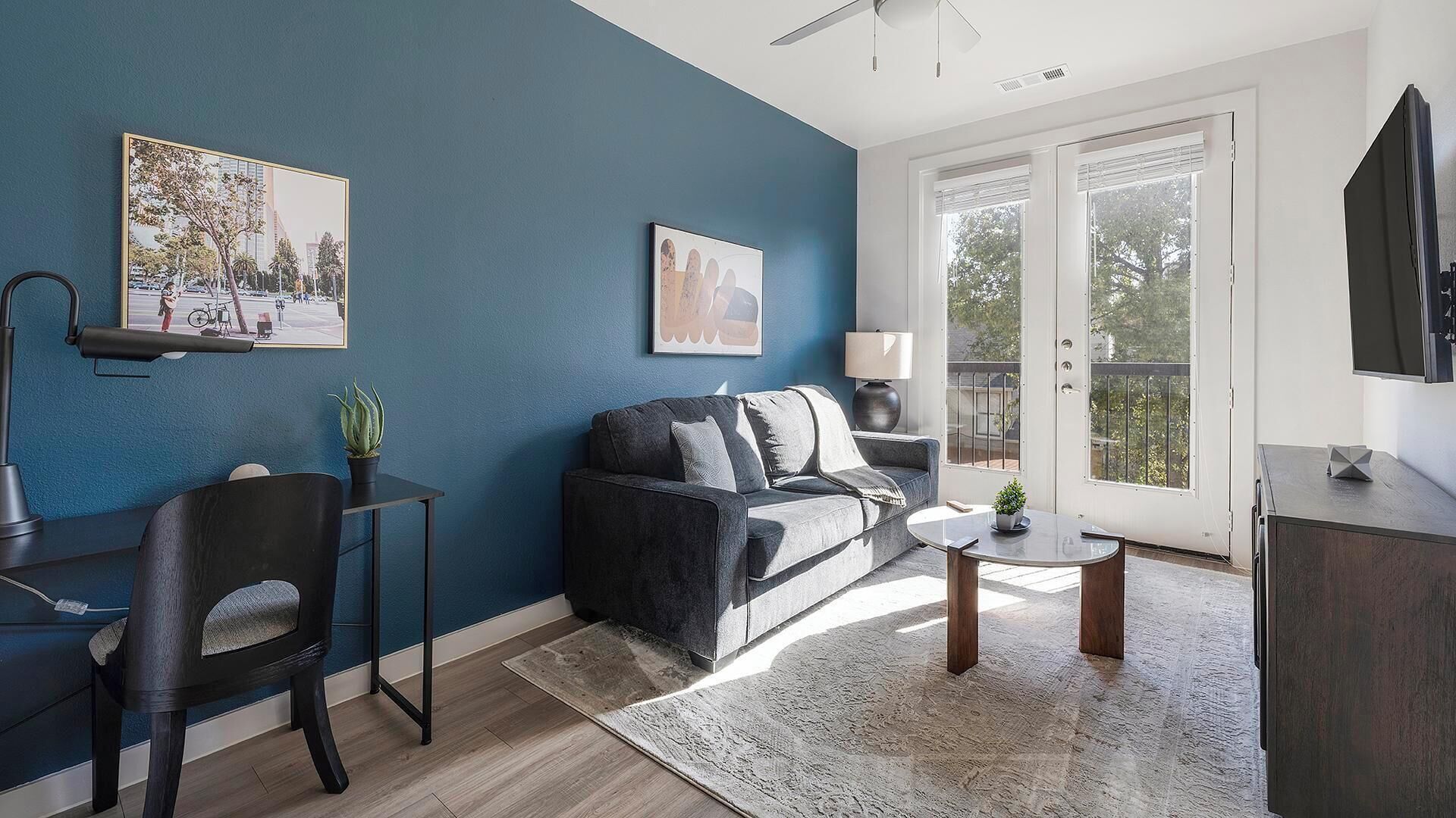 A modern living room with a dark blue accent wall, a grey sofa, a small round table, and a black chair.