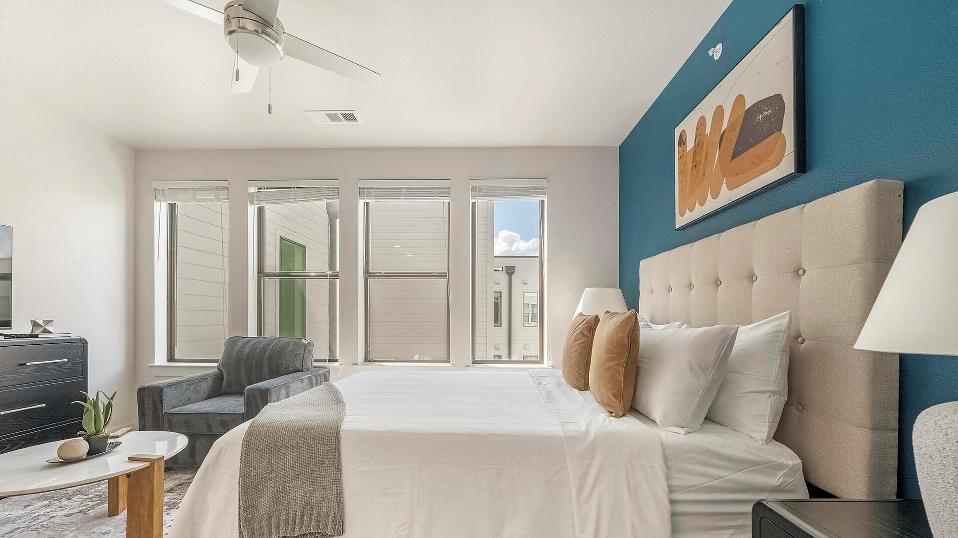 A modern hotel room with a large bed, a desk, a chair, and a ceiling fan.