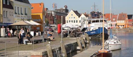 A waterfront area with boats docked, a pedestrian walkway, and buildings with commercial establishments.