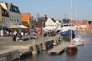 A waterfront area with boats docked, a pedestrian walkway, and buildings with commercial establishments. - Hekmat Apartments Fernsicht Schobüll (Husum)
