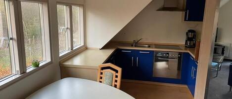 A kitchen with a dining table, blue cabinets, and a window with a view of trees.