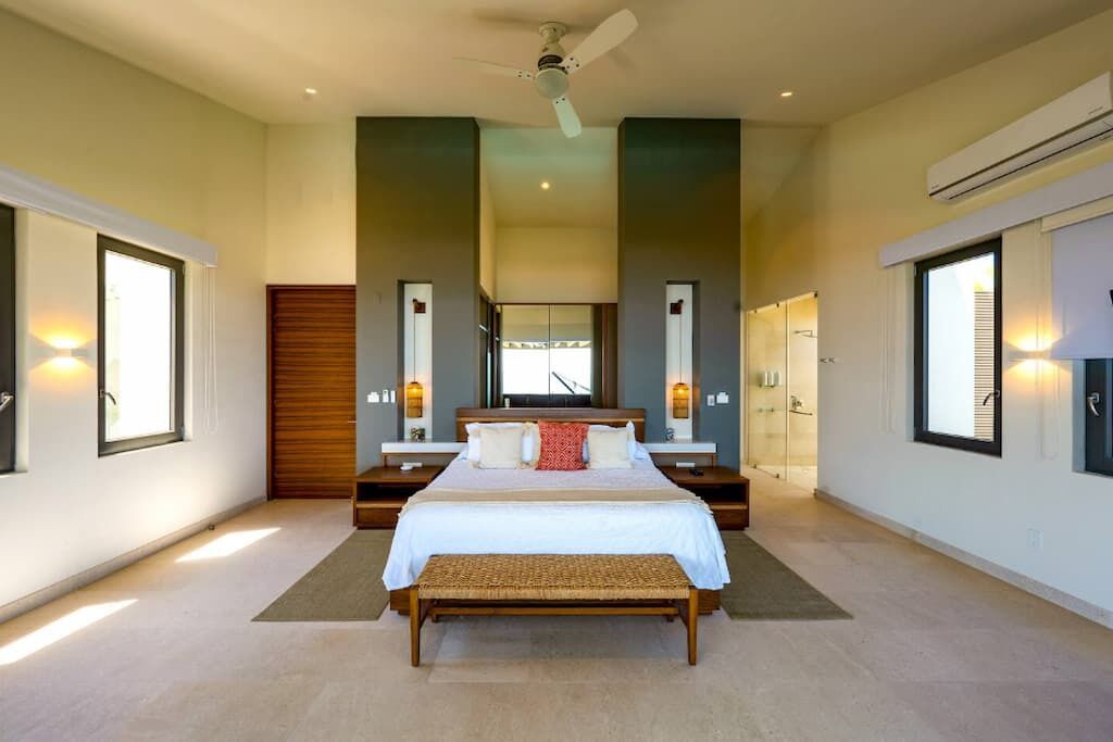 A spacious bedroom with a large bed, a ceiling fan, and a view of the city through large windows.