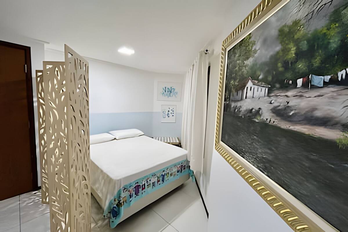 Quarto com cama, pintura de paisagem e divisória decorativa.