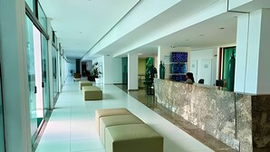 A long, modern hallway with a reception desk, seating areas, and a view of the interior. - Luxor Tambaú (João Pessoa)