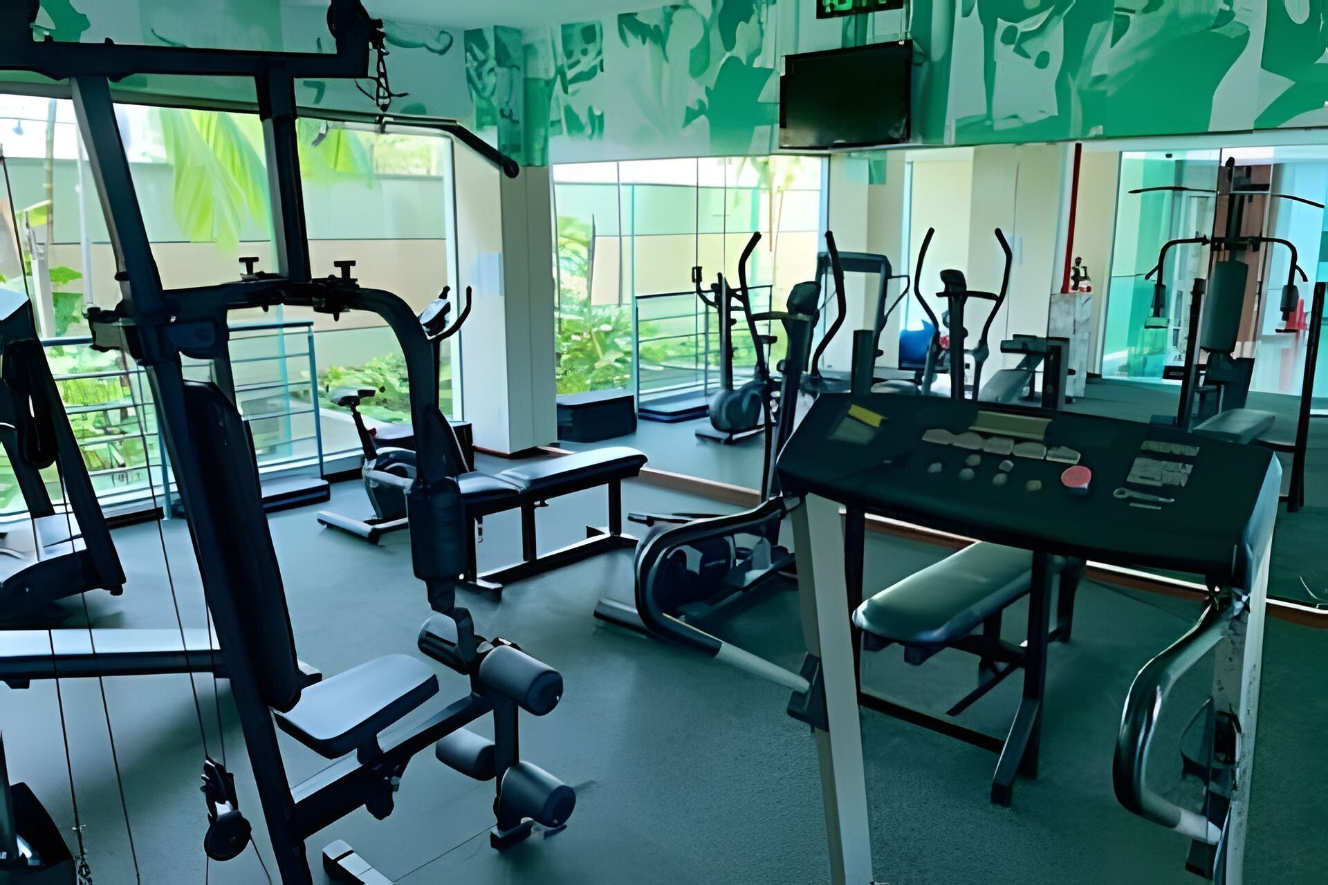 Ein Fitnessraum mit verschiedenen Trainingsgeräten, großen Fenstern und einer Bedienkonsole.