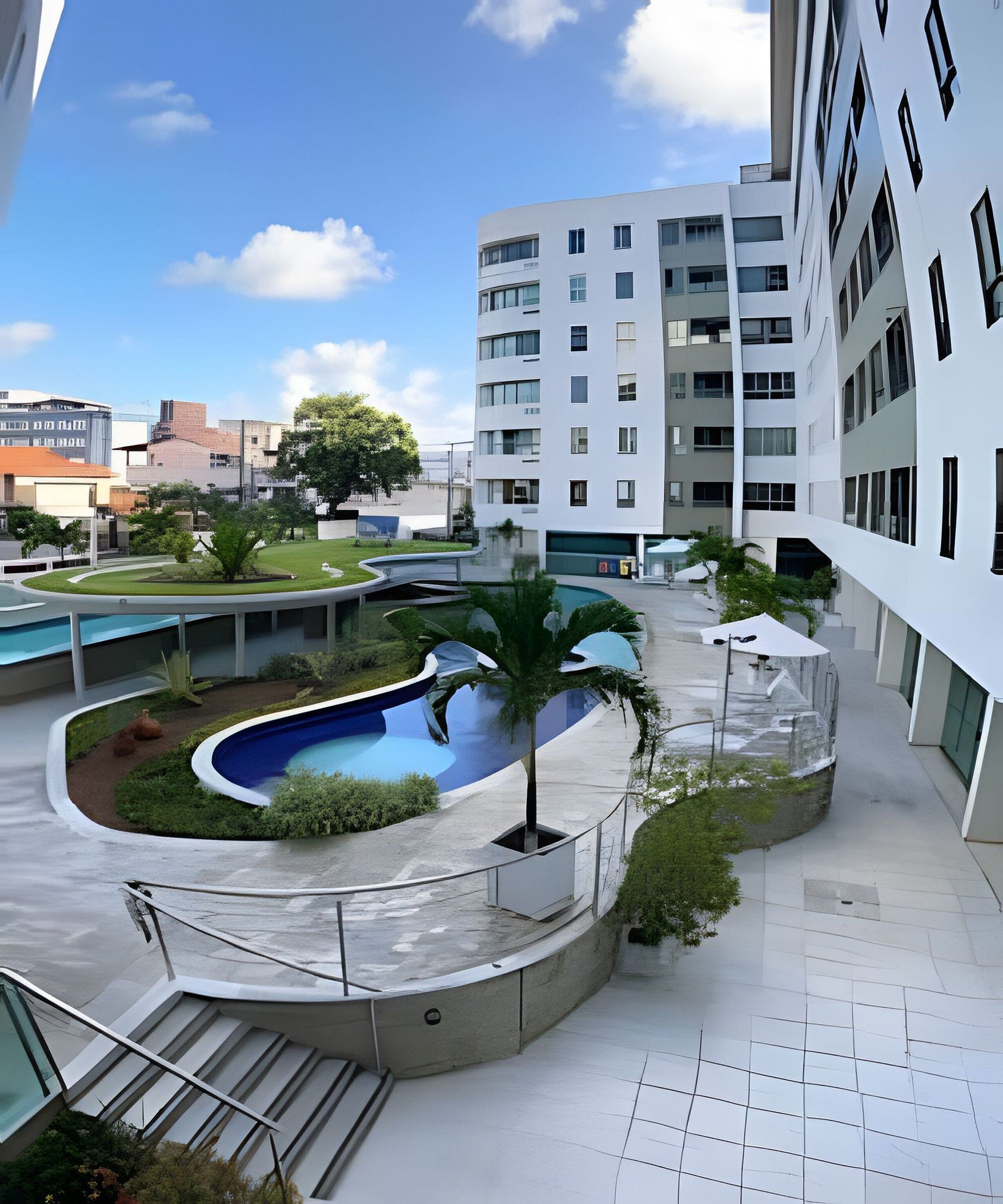 Un bâtiment moderne doté d’une piscine, entouré de verdure et surplombant un ciel dégagé.