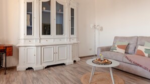 Un salon avec un meuble blanc, un canapé gris et une petite table ronde sur laquelle est posée une bougie.