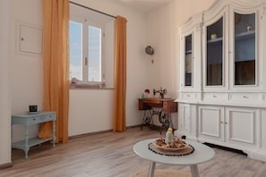 Ein Zimmer mit Holzboden, einem weißen Schrank mit Glastüren, einer Nähmaschine, einem kleinen Tisch mit Speisen und einem Fenster mit Vorhängen.