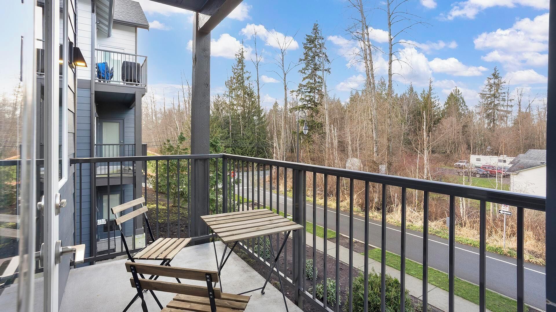A balcony with a table and chairs, overlooking a road with trees and a clear sky.