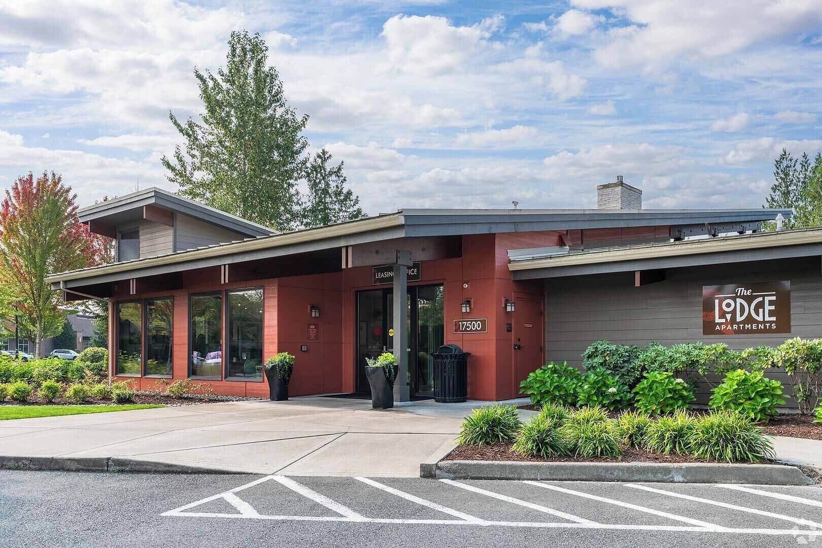 A LEASING office with a modern design, a parking lot, and landscaped areas with shrubs.