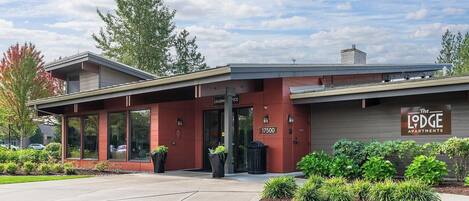 A LEASING office with a modern design, a parking lot, and landscaped areas with shrubs.