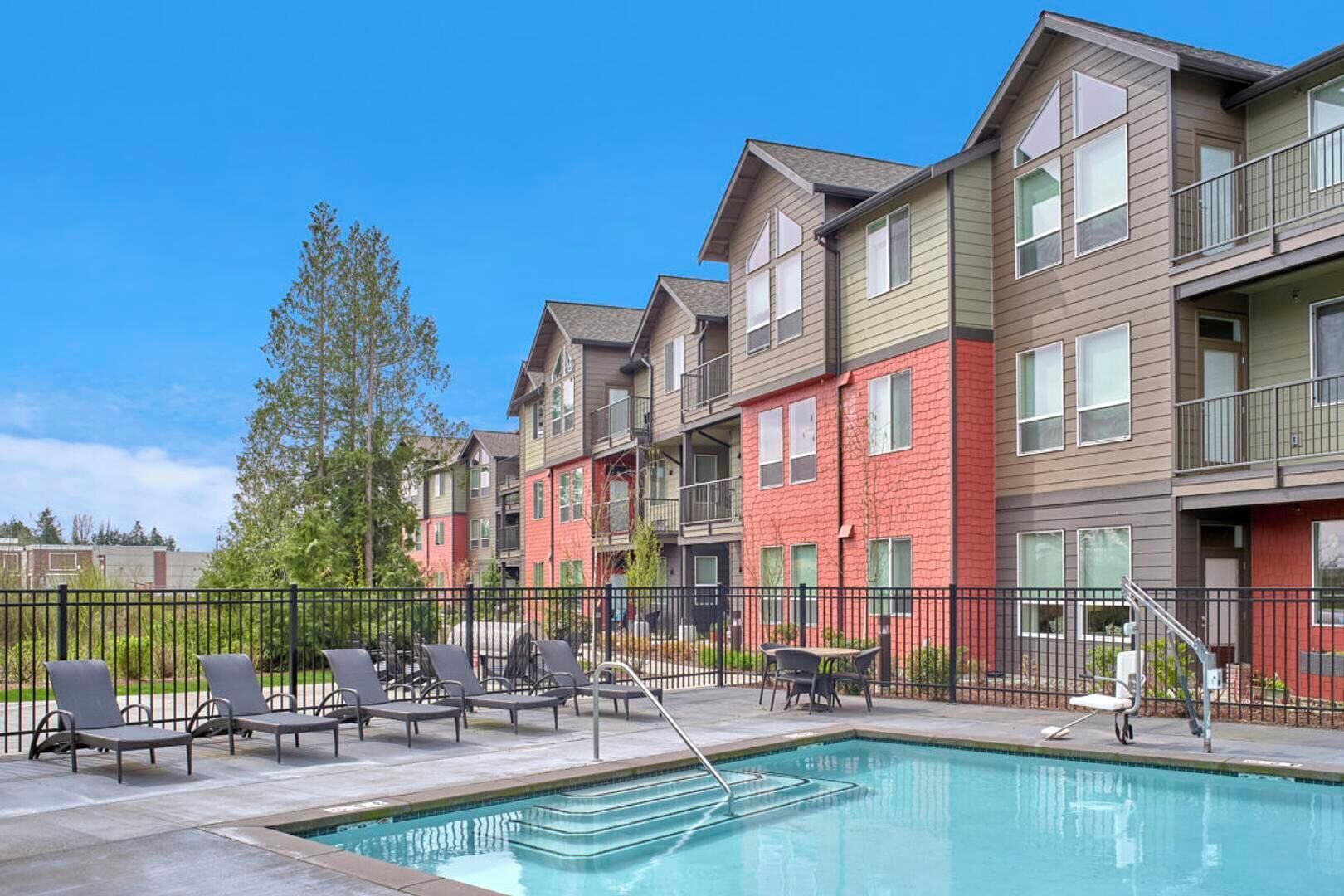 A residential building with a swimming pool, outdoor seating, and a fenced patio area.