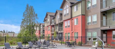 A residential building with a swimming pool, outdoor seating, and a fenced patio area.