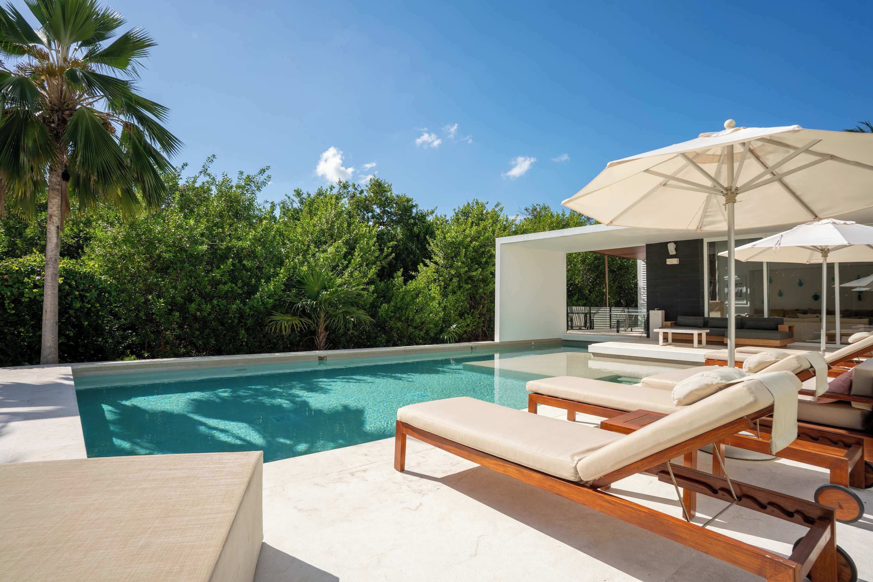 A pool area with lounge chairs and umbrellas, surrounded by lush greenery.