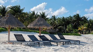 Een strand met vier ligbedden onder rieten parasols, omringd door palmbomen.