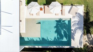 An aerial view of a modern pool area with a rectangular pool, surrounded by white umbrellas and lounge chairs.