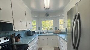 A kitchen with white cabinets, a stainless steel refrigerator, a black stove, and a window with a view of trees. - Charming Mill Beach Cottage by the Sea (Brookings)