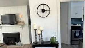 A living room with a fireplace, a television, and a dining area with a kitchen in the background. - Charming Mill Beach Cottage by the Sea (Brookings)