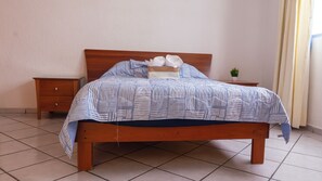 Una cama bien hecha con una colcha a rayas, dos almohadas y una mesita de noche con una planta.