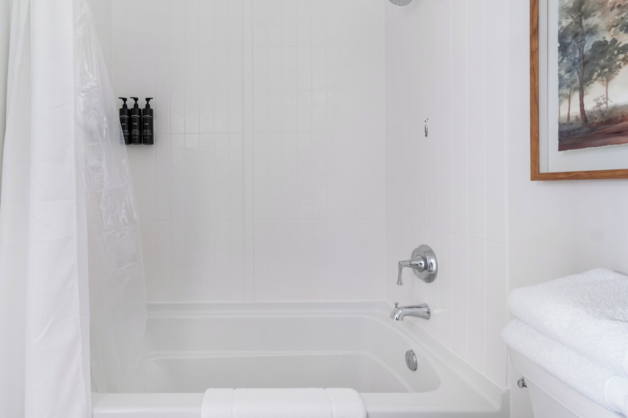 A bathroom with a bathtub, a shower curtain, and a painting on the wall.