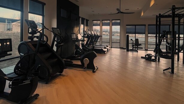 A spacious gym with various cardio machines, weightlifting equipment, and large windows offering views of the outdoors. - Landing Furnished Apartments - Billings, MT (Billings)