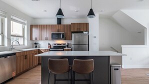 A modern kitchen with wooden cabinets, stainless steel appliances, and a central island with bar stools. - Landing Furnished Apartments - Billings, MT (Billings)