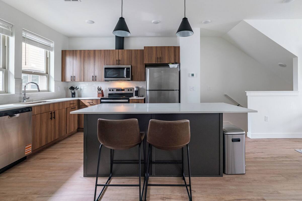 A modern kitchen with wooden cabinets, stainless steel appliances, and a central island with bar stools.