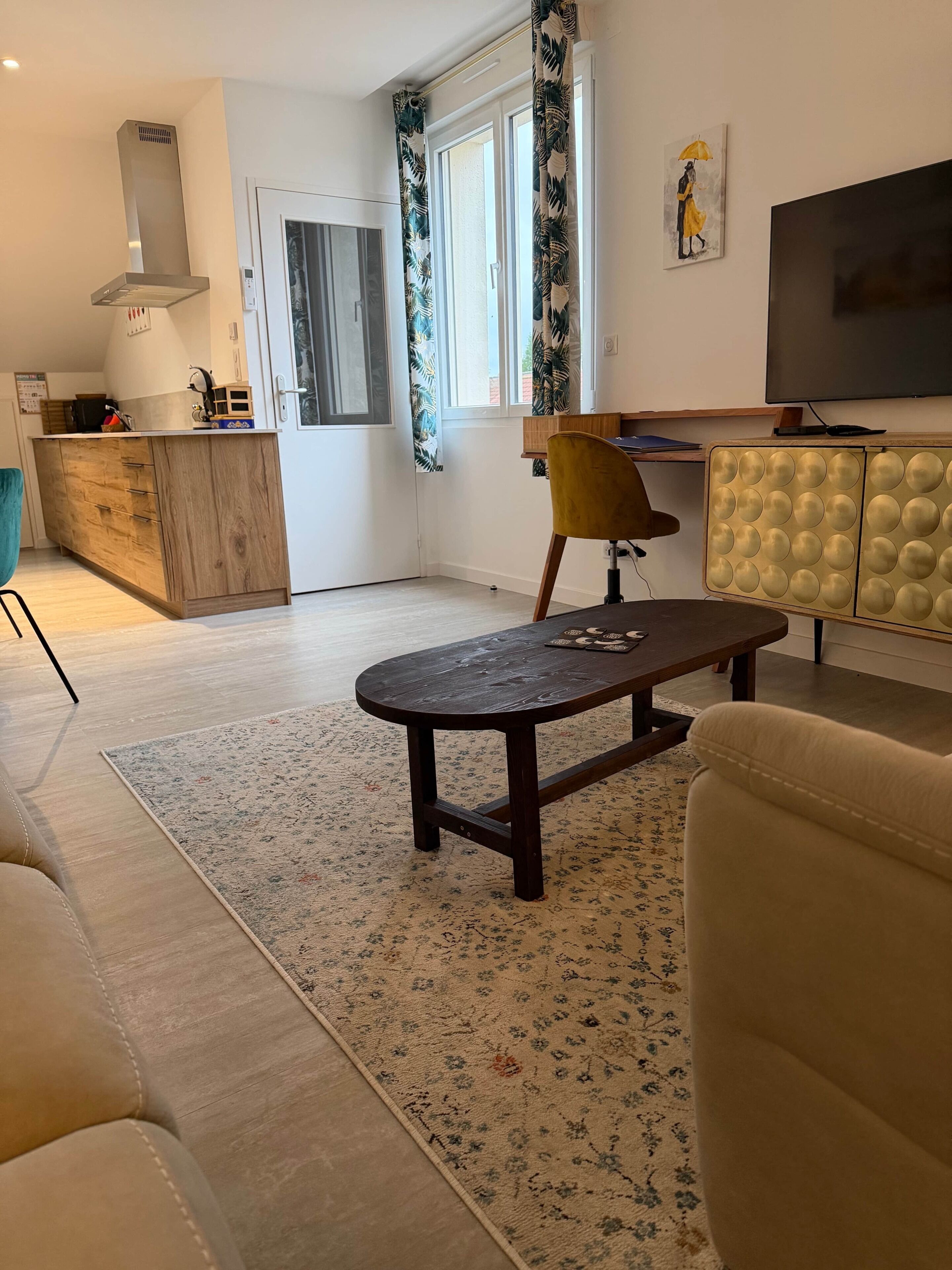 Un salon comprenant un canapé, une table basse, un téléviseur, un meuble en bois et une fenêtre avec des rideaux.