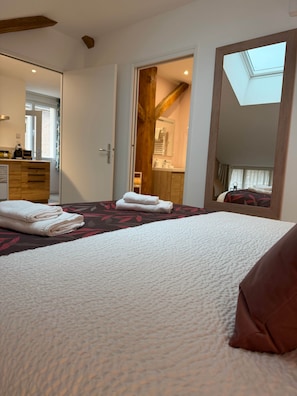 A hotel room with a bed, a bathroom, a mirror, and a skylight.