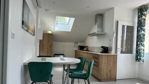 A modern kitchen with a central island, a dining area with green chairs, and a skylight.