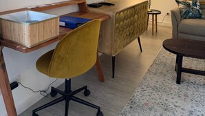 A modern living room with a flat-screen TV, a wooden desk, a yellow chair, a sofa, and a patterned rug.