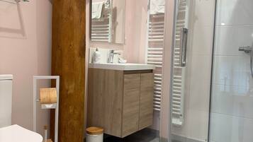 A bathroom with a toilet, sink, mirror, wooden beam, and a glass shower enclosure.