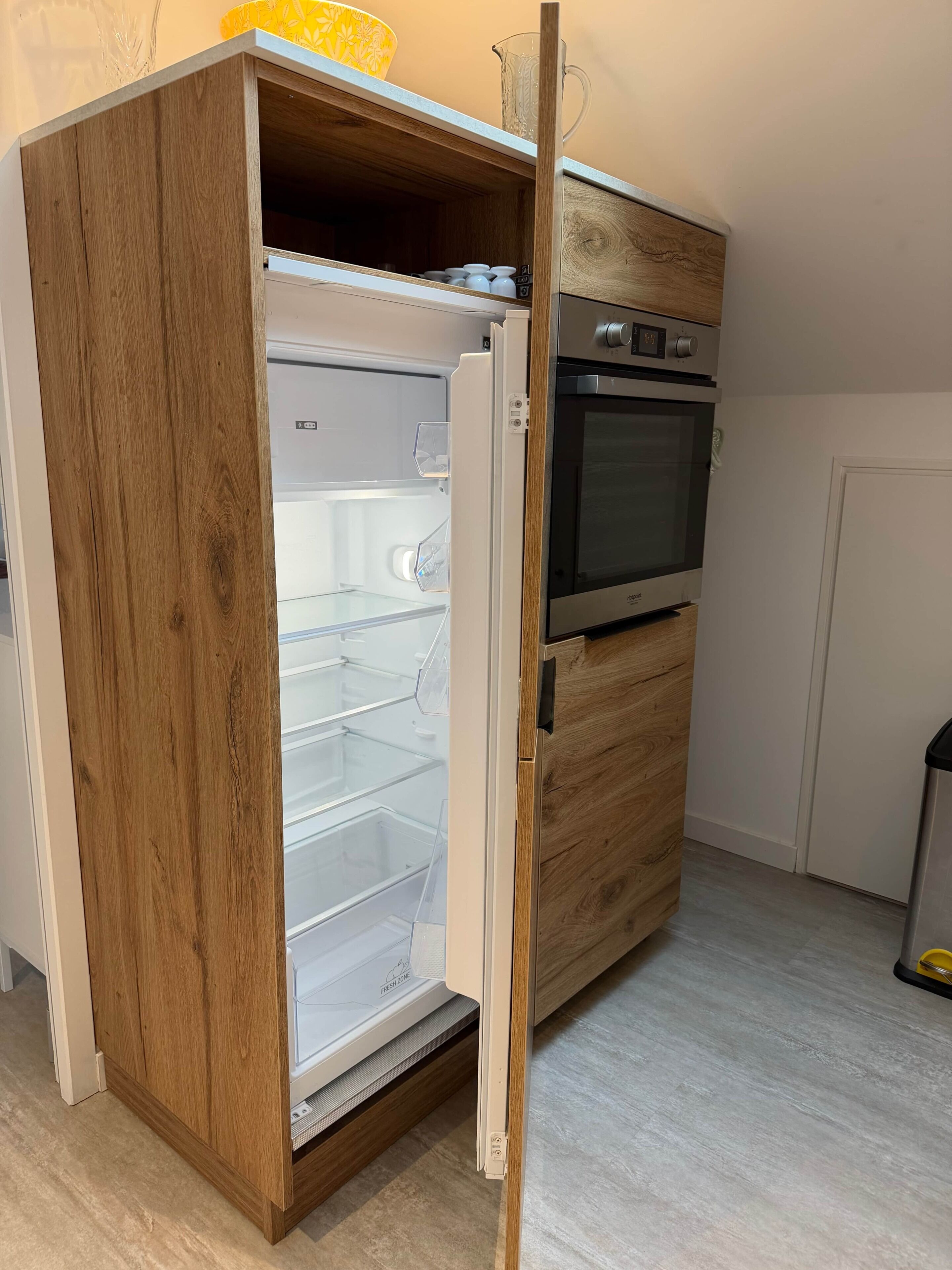 Una cocina con horno empotrado, microondas y un mueble de madera con cajón congelador.