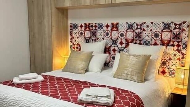 Ein Bett mit einer rot-weißen Bettdecke, einem Holzkopfende und mehreren Kissen.