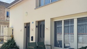 Un edificio con fachada plana, una puerta numerada con el 46, y un pequeño espacio exterior con sillas y una mesa.