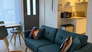Ein modernes Wohnzimmer mit einem türkisblauen Sofa, einem Holztisch und einem Essbereich mit Tisch und Stühlen.